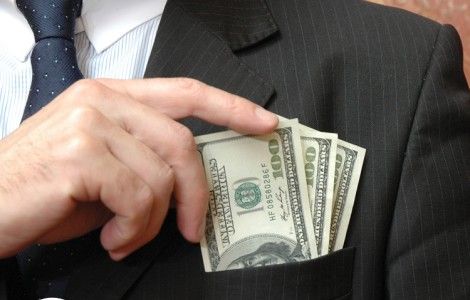 closeup of man putting hundred-dollar bills into his suit jacket pocket