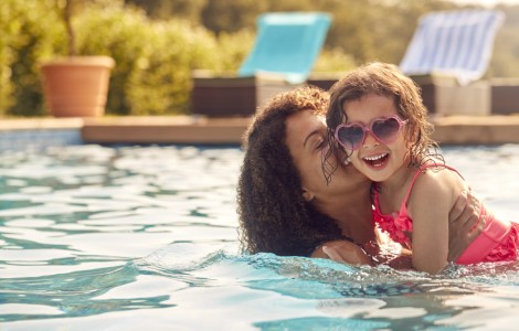 mother and young daughter swimming together in pool and smiling