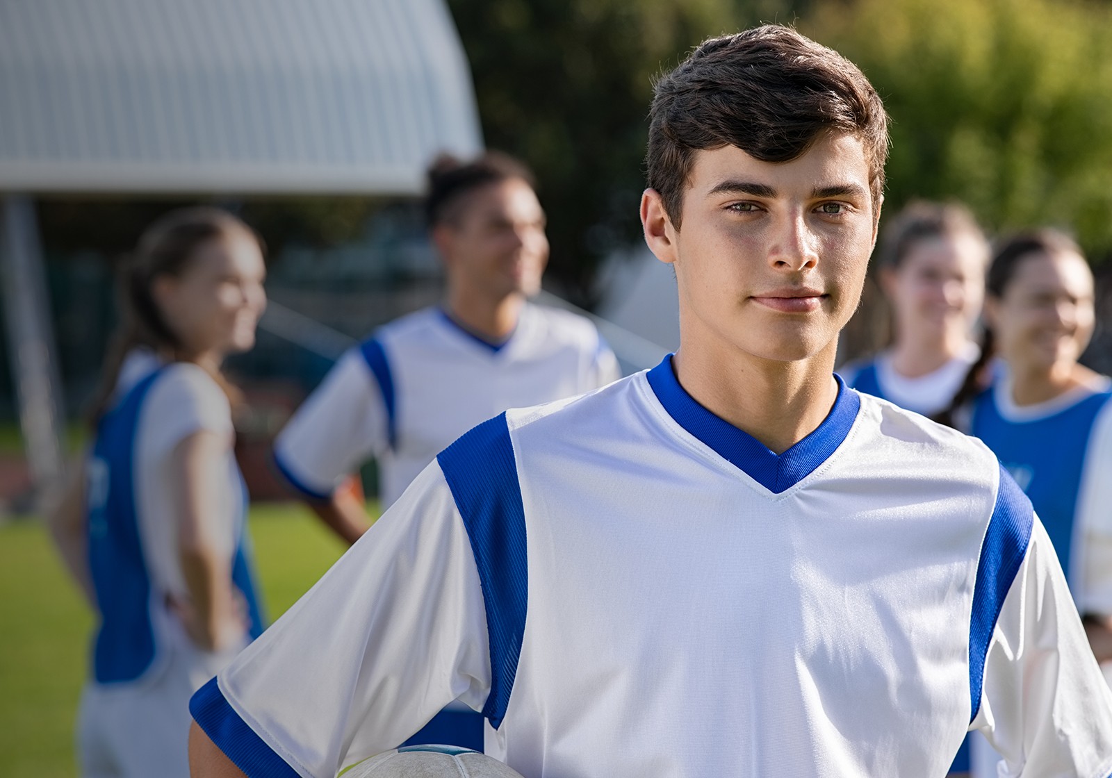 teenage boy in athletic uniform outside in front of team looking at camera