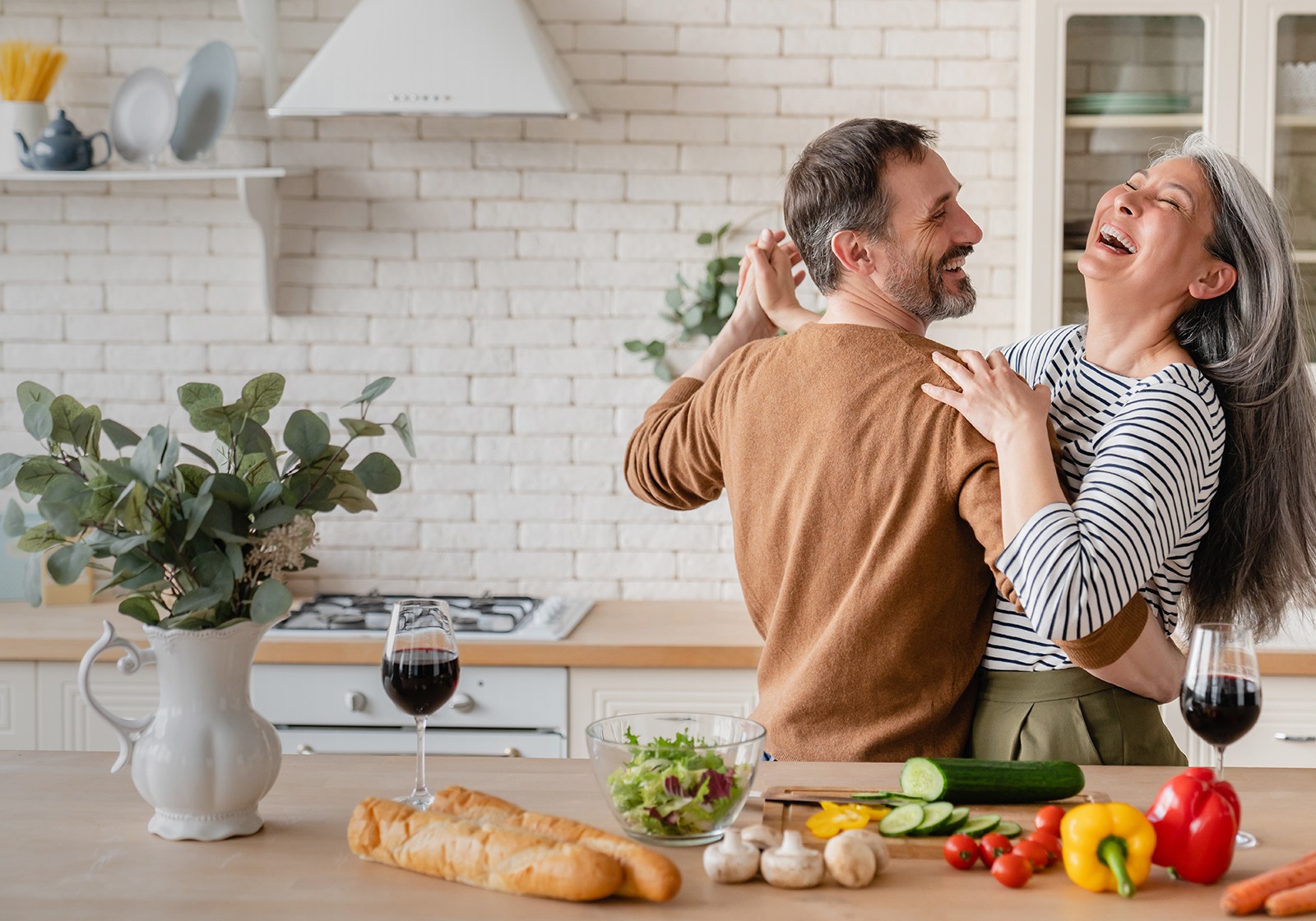 middle aged couple slow dancing together in their kitchen while laughing