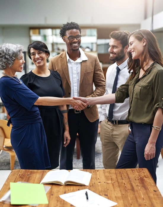 2 people in office shake hands while 3 more onlookers smile