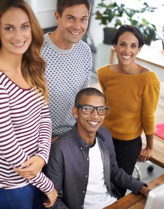 4 people in a casual office environment looking at the camera and smiling