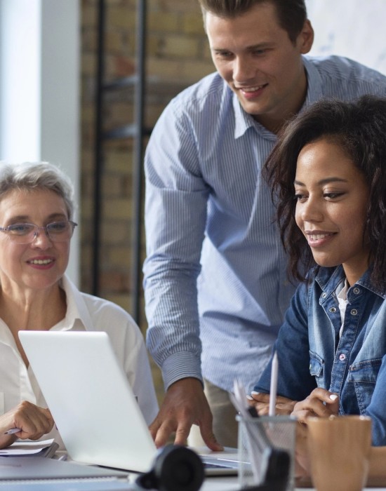 man in casual office environment helping colleague on her laptop while another onlooker observes